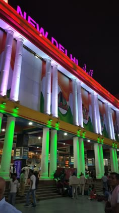 people are walking around in front of a building with columns and pillars lit up at night