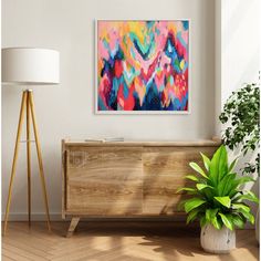 an abstract painting hangs on the wall next to a potted plant in a living room