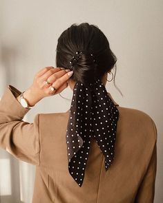 a woman wearing a brown jacket and black polka dot print scarf around her neck, with one hand on her head