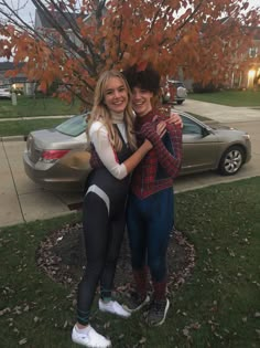 two girls are hugging in front of a tree and car on the side of the road