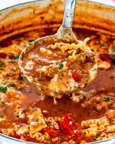 a ladle full of macaroni and cheese being lifted from a pot filled with tomato sauce