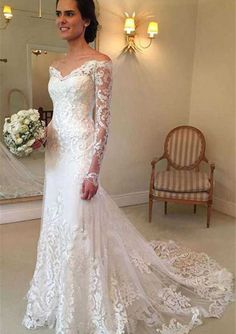 a woman standing in front of a mirror wearing a wedding dress with long sleeves and lace