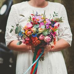 a woman holding a bouquet of flowers in her hands with a rainbow ribbon around it