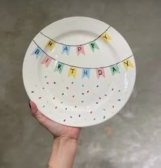 a hand holding a happy birthday plate with confetti and streamers on it