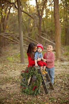 two young children sitting on top of a ladder in the woods with christmas wreaths