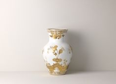 a white and gold vase sitting on top of a table next to a gray wall