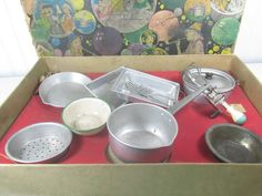 an assortment of cooking utensils and pans in a cardboard box on a table