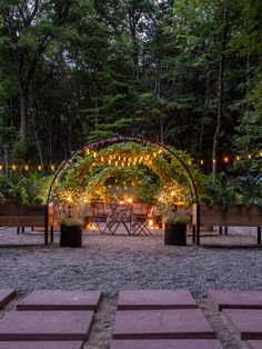 an outdoor wedding venue with lights and greenery on the back wall, surrounded by wooden benches