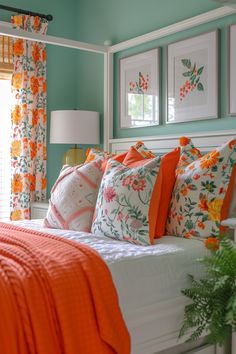 a bed with orange and white pillows in a bedroom next to two framed pictures on the wall