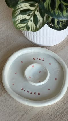 a white ceramic dish with the word girl on it next to a potted plant