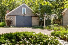 a house with two garages in the front and one on the other side, surrounded by greenery