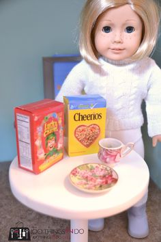 a doll is sitting at a table with cereal and a tea cup on it, next to a box of cheetos