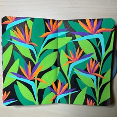 an open notebook with brightly colored flowers and leaves on the cover, sitting on a table