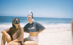 two women sitting on the beach with snorkels in their mouth and one wearing a diving mask