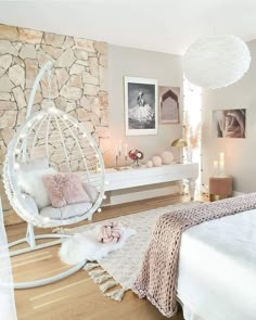 a bedroom with a white bed and hanging chair next to a stone wall in the corner