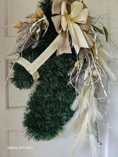 a wreath hanging on the front door decorated with pine cones, feathers and ribbon bows