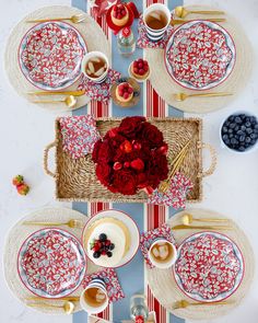 the table is set with red and white plates, silverware, cups, and flowers