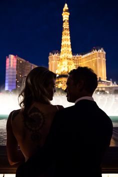 a man and woman standing next to each other in front of the eiffel tower