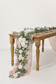 a wooden bench with flowers and greenery on the top, along with a pink scarf draped over it