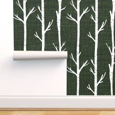 the wallpaper is designed with white trees on dark green fabric, and it has a roll of paper in front of it