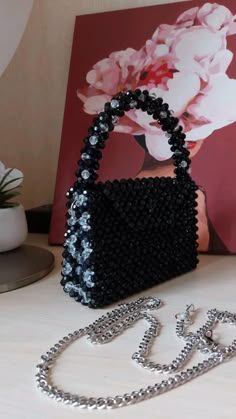 a black purse sitting on top of a table next to a white vase filled with flowers