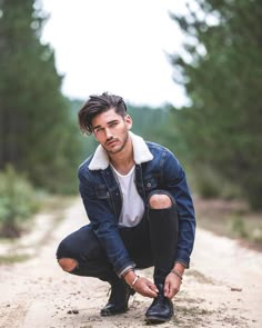 a man squatting down on a dirt road with his foot in the air and wearing black shoes