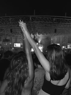 two women holding their arms in the air at a concert