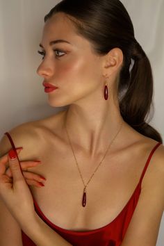 a woman in a red dress is holding her hand up to her chest and looking off into the distance