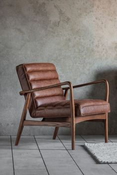 two brown leather chairs sitting next to each other on top of a white rug in front of a gray wall