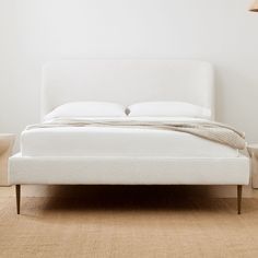 a white bed sitting on top of a wooden floor next to a lamp and table