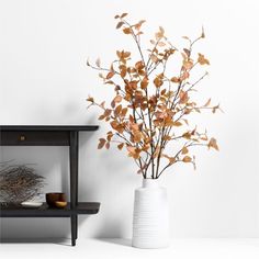 a white vase filled with lots of brown leaves next to a wall mounted shelf on the wall