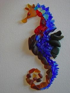 a seahorse made out of glass sitting on top of a white wall next to rocks