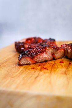 two pieces of meat sitting on top of a wooden cutting board with ketchup