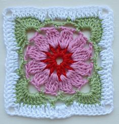 a crocheted square with a red flower in the center and green border around it