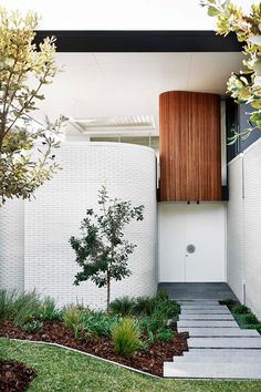 a modern house with white brick walls and green plants in the front yard, next to a small tree