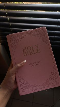 a person holding up a pink bible in their hand