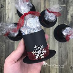 someone is holding up some candy wrapped in black paper and red ribbon with white snowflakes on it