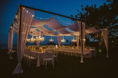 an outdoor dining area is lit up at night with lights strung over the tables and chairs