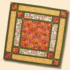 an orange and green quilted square with flowers on the center is sitting in front of a white wall