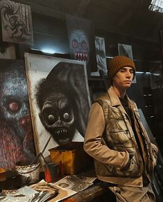 a man is standing in front of some paintings and looking at the camera while wearing a beanie