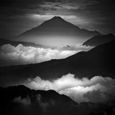 black and white photograph of mountains with clouds below them in the distance, taken from an airplane