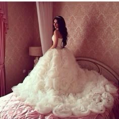 a woman in a white wedding dress sitting on a bed with pink walls and curtains