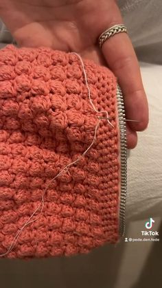 a person is holding an orange crochet purse with white thread on it and there are two silver rings around the edge