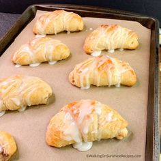 six croissants on a baking sheet with icing drizzled