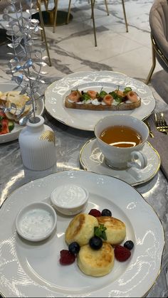 two plates with food on them sitting on a table next to cups and saucers