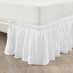 a white bed skirt with ruffles on the bottom and bottom, in front of a wooden floor