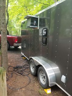 a trailer parked in the woods next to a red pickup truck and another silver vehicle