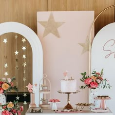 a table topped with cakes and desserts on top of a white table covered in pink flowers