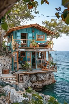 a blue house sitting on top of a rock cliff next to the ocean with stairs leading up to it