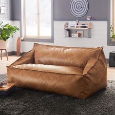 a large brown leather couch sitting on top of a carpeted floor next to a window